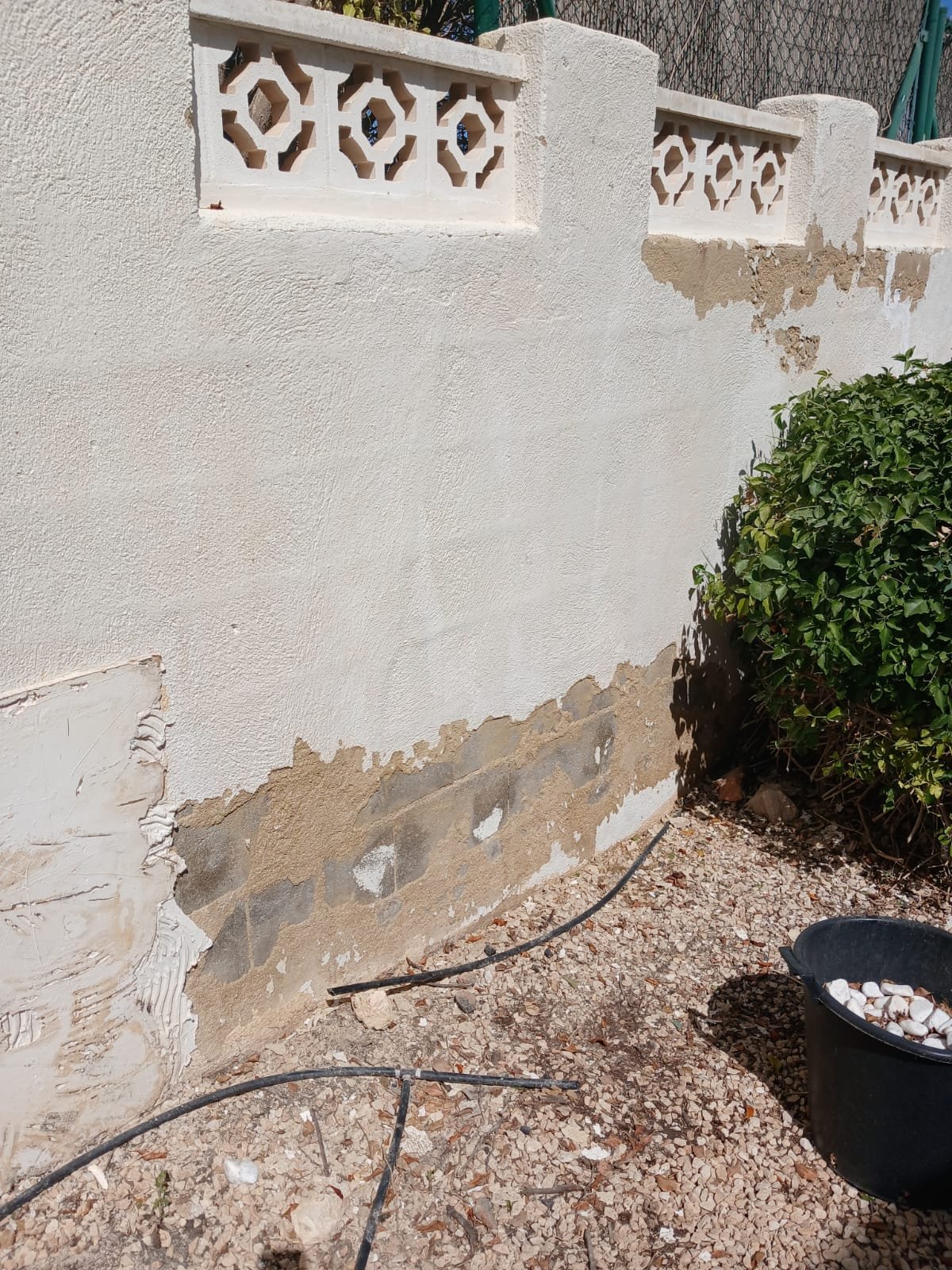 A garden boundary wall mid-repair, old render stripped back ready for patching