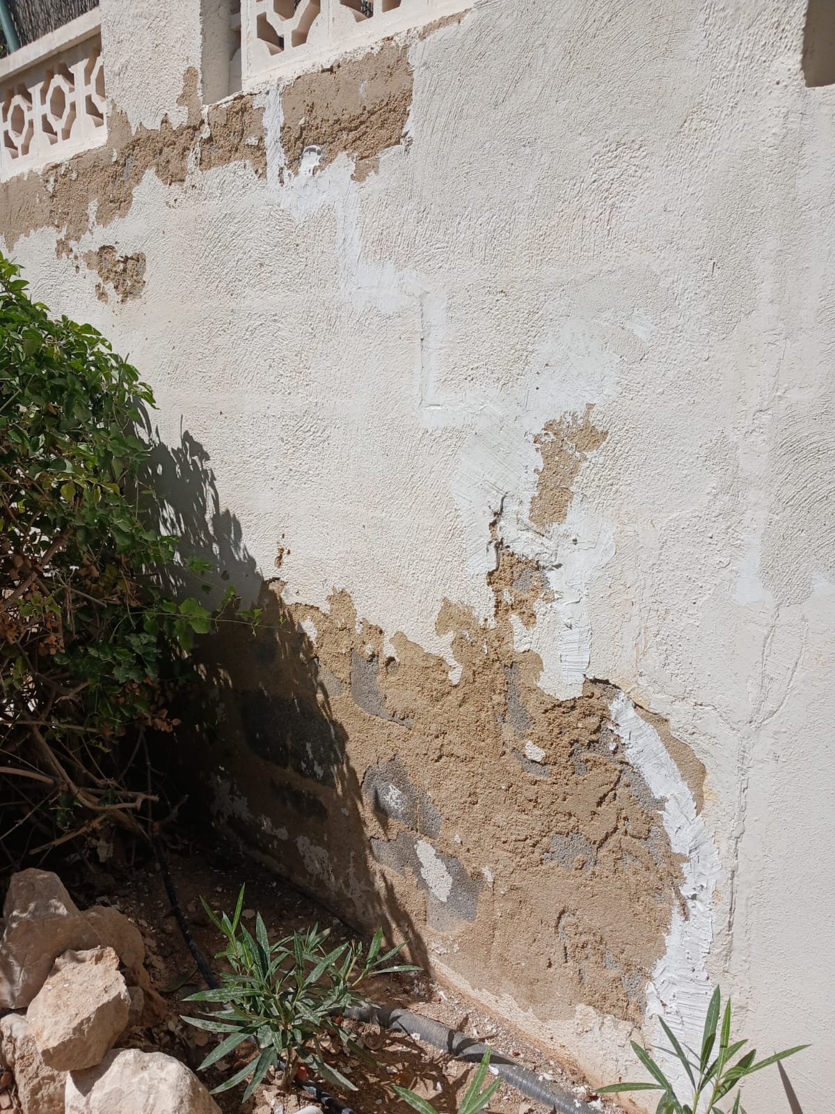 Close-up of an exterior wall mid-repair, old render patched with fresh plaster ahead of painting